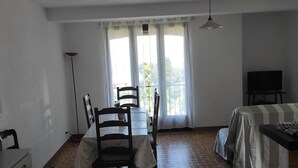 Ein Zimmer mit Esstisch, Stühlen, Fernseher und einem Bett mit gestreifter Bettwäsche.