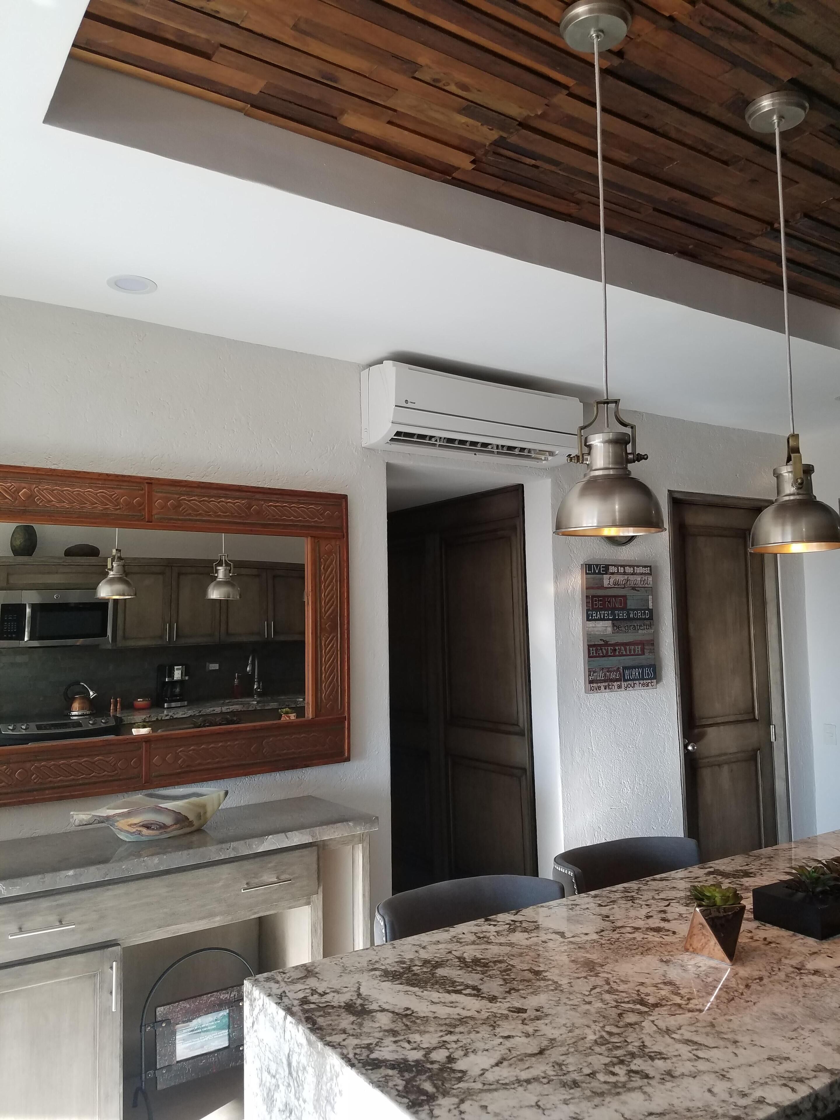 A kitchen with wooden cabinets, a marble countertop, pendant lights, and an air conditioning unit.