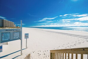 Una playa con un cartel que muestra banderas de advertencia y un paseo marítimo de madera.