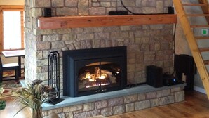 A stone fireplace with a TV mounted above it, a wooden staircase to the right, and a sofa in the foreground. - Beautiful Chalet Style Home with Seasonal Mountains Views in North Conway, NH (North Conway)
