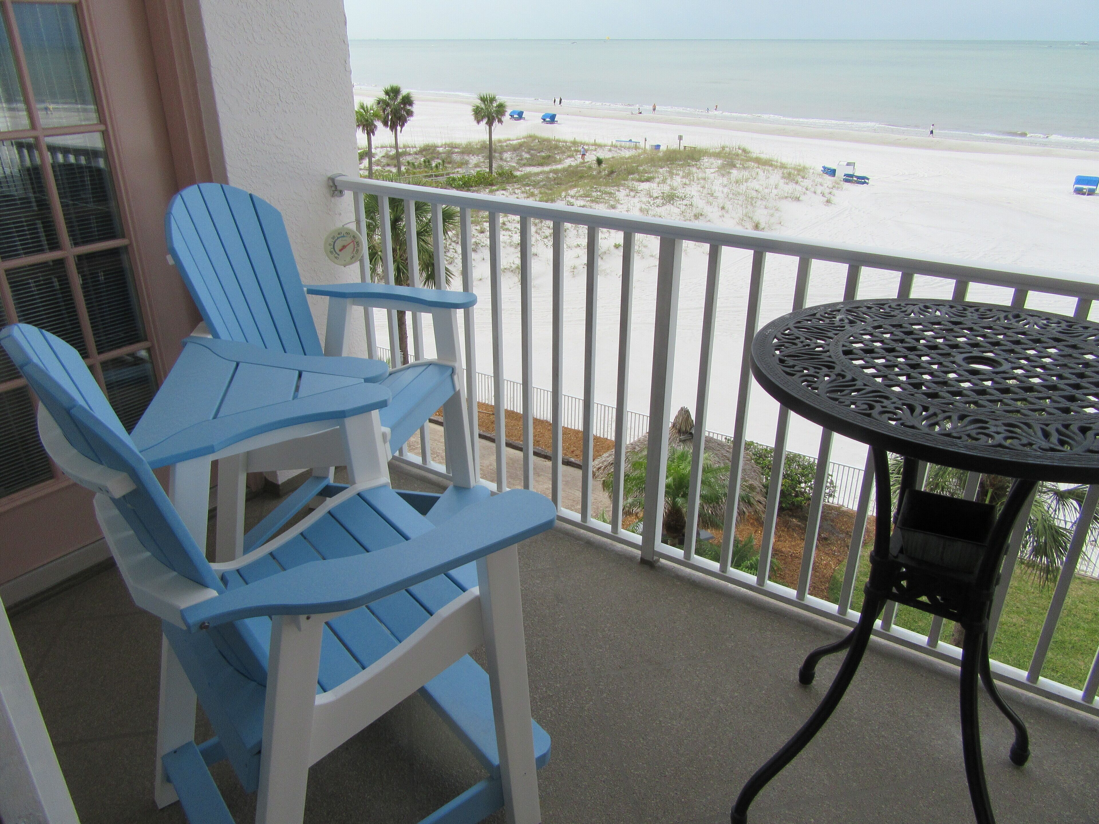 A balcony with two blue Adirondack chairs and a round metal table.