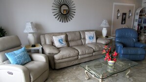 Ein Wohnzimmer mit einem beigefarbenen Sofa, einem blauen Sessel, einem Glastisch und einem blauen Sessel.