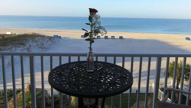 Ein Balkon mit Blick auf einen Strand, ein Tisch mit Blumenvase und einige blaue Stühle.