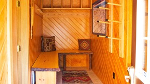 Un interior de madera con un banco, cojines, un tapete estampado y un cuadro en la pared.