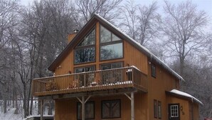 Una cabaña de madera con balcón, ventanas amplias y un paisaje cubierto de nieve.
