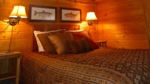 Un dormitorio de cabaña de madera acogedor, con una cama, dos lámparas de pared y cuadros de peces enmarcados.