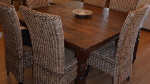 A dining area with a wooden table, wicker chairs, a chandelier, and a television in the background. - Beachfront condo: Create some memories! (South Padre Island)