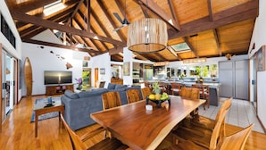 A spacious living area with a wooden dining table, a sofa, and a TV. - Maka Nui Estate/ Luxury Big Island Ocean View Home Above Kealakekua Bay (Captain Cook)