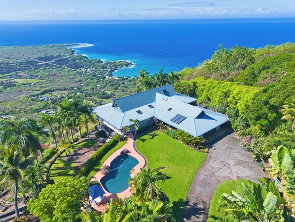 A large house with a swimming pool, surrounded by lush greenery and overlooking a coastline. - Maka Nui Estate/ Luxury Big Island Ocean View Home Above Kealakekua Bay (Captain Cook)