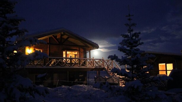 Eine Holzhütte mit Balkon, umgeben von schneebedeckten Bäumen.