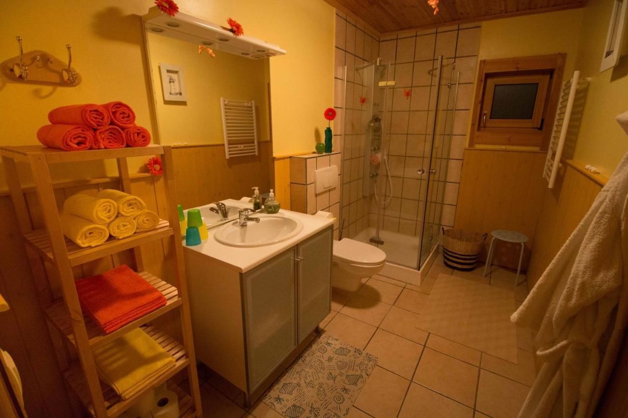 Un baño con lavamanos, inodoro y ducha. Hay toallas en estantes y una alfombra de baño en el suelo.
