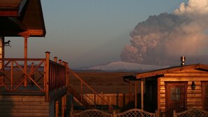 Eine Holzhütte mit einem Balkon mit Blick auf eine verschneite Landschaft und einer großen Wolkenformation in der Ferne.