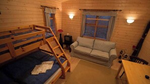 Ein kleines Zimmer mit Etagenbetten, einer Schlafcouch, einem kleinen Tisch und zwei fensterbepflanzten Fenstern.