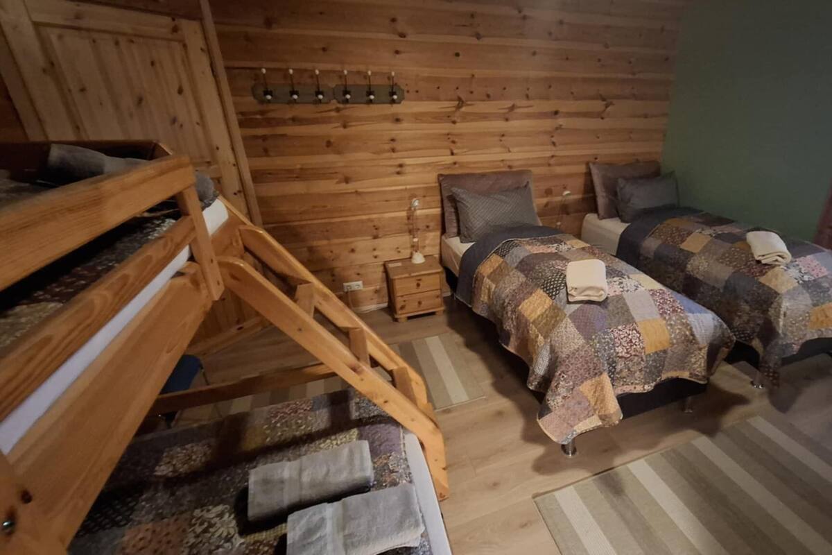 Una habitación estilo cabaña con literas, dos camas individuales, una pared de madera, una ventana con persianas y una mesita de noche pequeña.