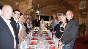 Eine Gruppe von Personen steht an einem langen Esstisch mit weißen Tischdecken, roten Servietten und klaren Gläsern.