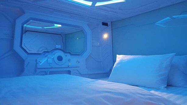 A futuristic room with a central control panel, a bed with white bedding, and a ceiling with a circular light fixture. - Avagard Capsule Hotel - Suvarnabhumi Airport (Bang Phli)