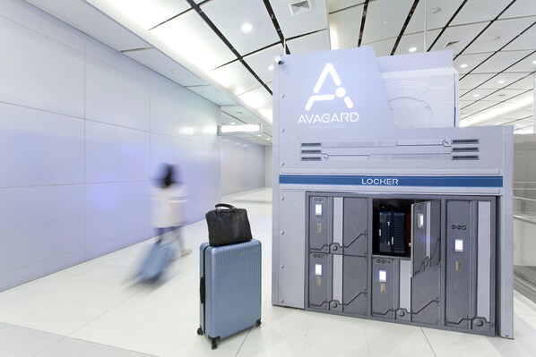An airport luggage storage area with lockers and a sign for the Avagard Capsule Hotel.