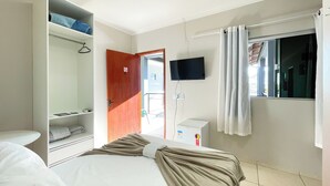 Une chambre d’hôtel avec un lit, une armoire, une télévision et une fenêtre avec des rideaux.