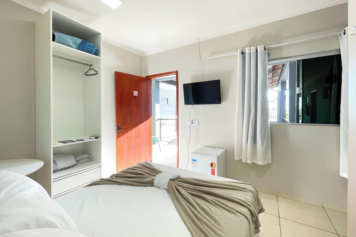 A hotel room with a bed, a wardrobe, a television, and a window with curtains.