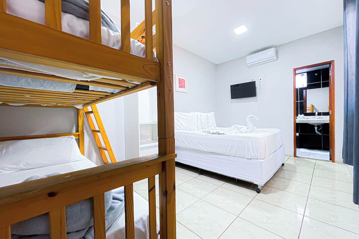A hotel room with bunk beds, a single bed, a TV, a bathroom with a mirror, and a tiled floor.