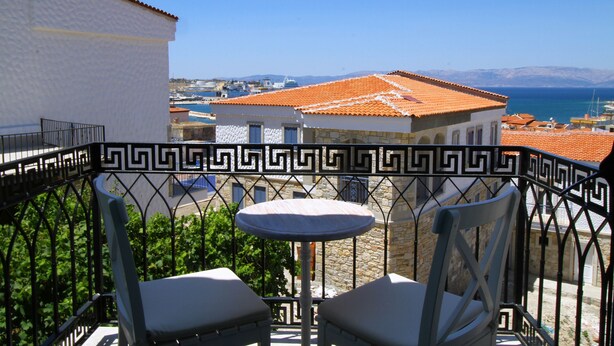 A balcony with a table and two chairs, overlooking a coastal town with buildings and a clear sky. - Cesme Kale Tas Apart (Cesme)