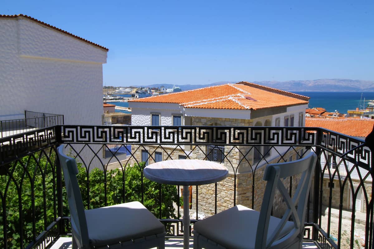 A balcony with a table and two chairs, overlooking a coastal town with buildings and a clear sky.