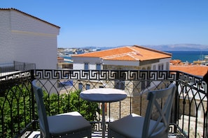 A balcony with a table and two chairs, overlooking a coastal town with buildings and a clear sky. - Cesme Kale Tas Apart (Cesme)