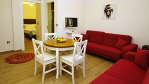 A living room with a red sofa, a dining table with chairs, a TV, and a painting on the wall. - Cesme Kale Tas Apart (Cesme)