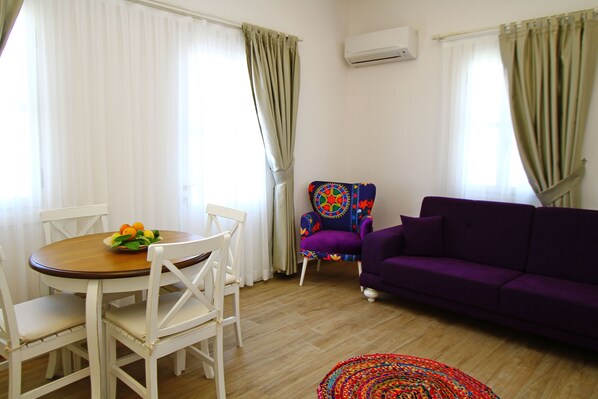A living room with a round wooden table, white chairs, a purple sofa, a colorful armchair, and a patterned rug. - Cesme Kale Tas Apart (Cesme)