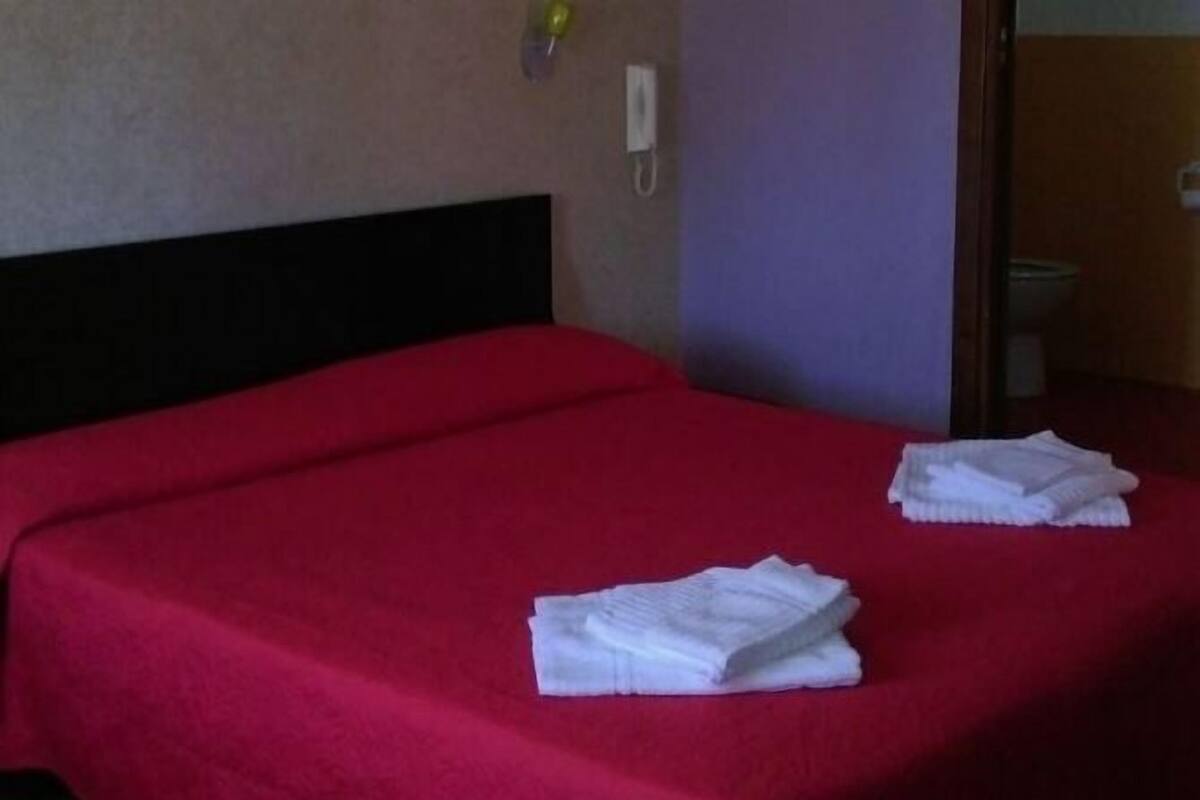 A hotel room with a red bedspread, a black headboard, and two folded white towels on the bed.