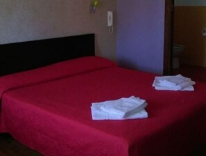Hotellihuone, jossa on punainen sängynpeite, musta pääty ja kaksi valkoista, taitettua pyyhettä sängyllä.
