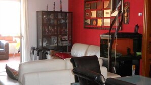 A living room with a white sofa, a black chair, a glass coffee table, and a red accent wall. - Olympus B&B (Agrigento)