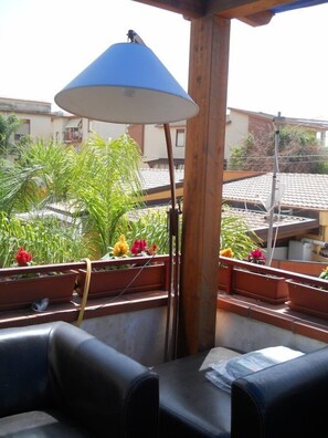Un balcon avec une lampe bleue, des plantes en pot et une vue sur les bâtiments voisins.