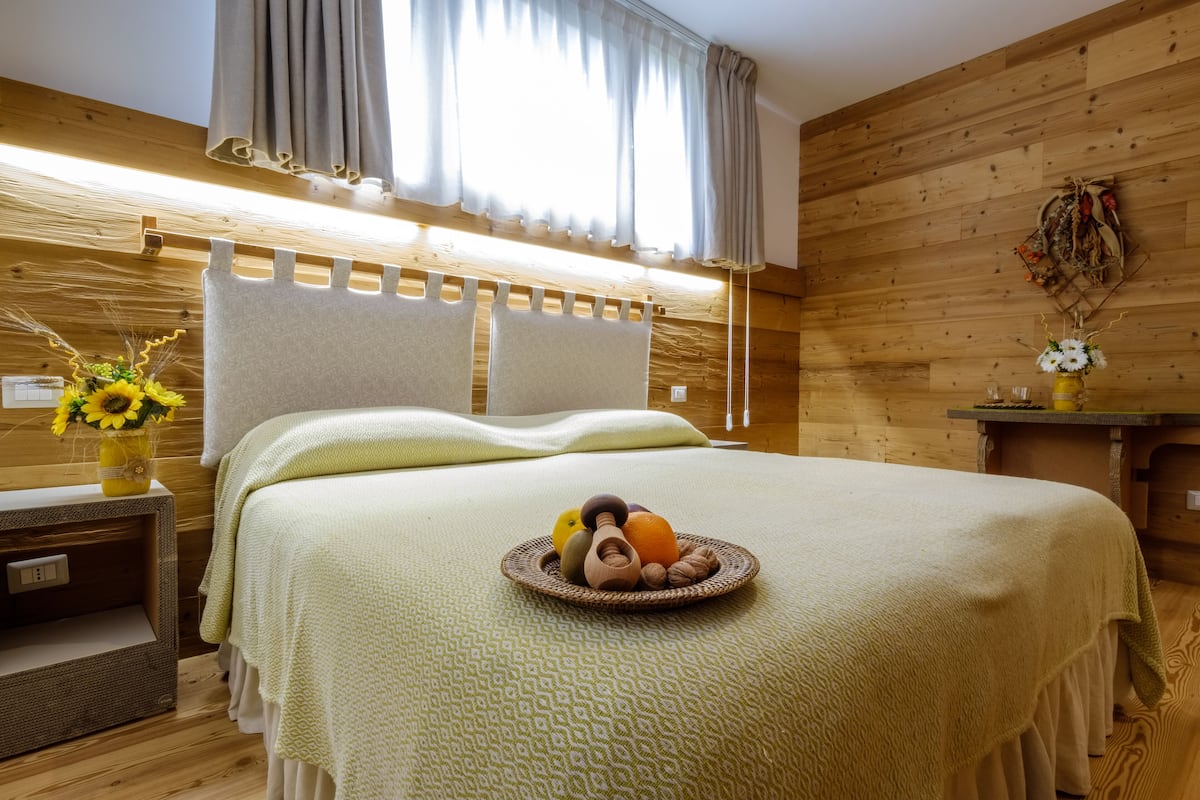 Una stanza in legno con un letto, un comodino, un vaso con fiori e un tavolino con una ciotola di frutta.
