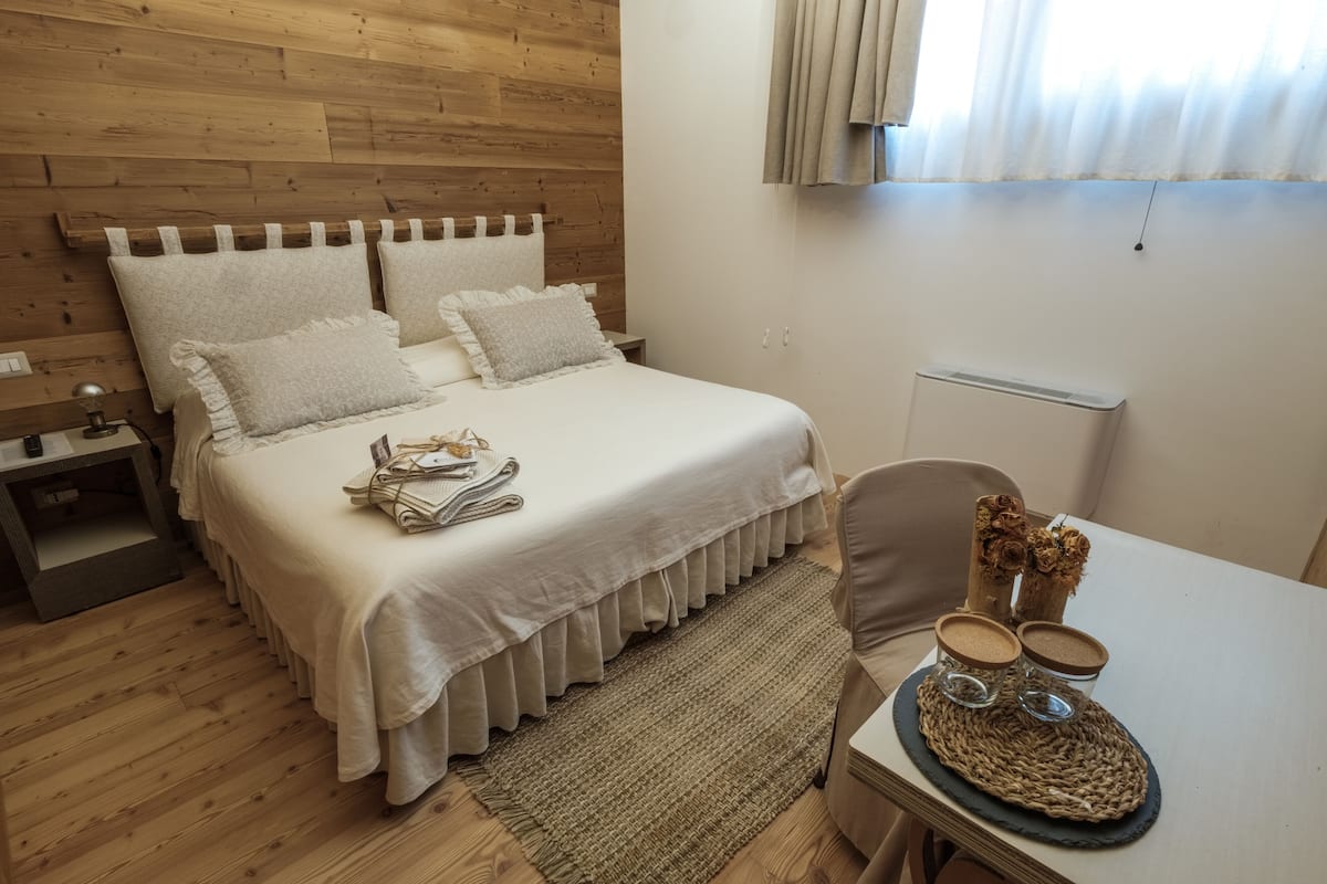 Una camera da letto ordinata con testiera in legno, un letto con biancheria da letto bianca, un piccolo comodino, una sedia e un tavolo con oggetti decorativi.