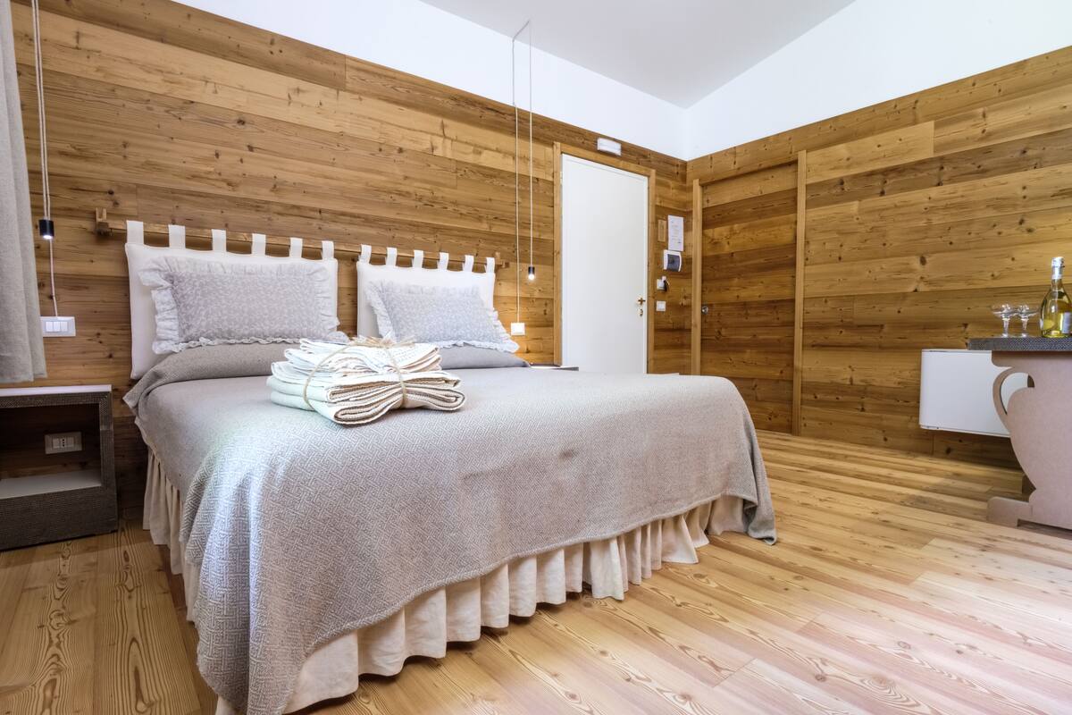 Una camera da letto con una testiera in legno, un letto con copriletto decorato, un comodino e un tavolino di fianco al letto.