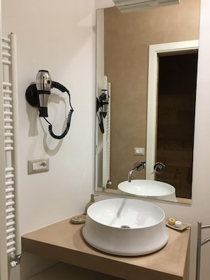 A bathroom with a white sink, a mirror, a hairdryer mounted on the wall, and a towel rack. - Bio & B Italyke (Viterbo)