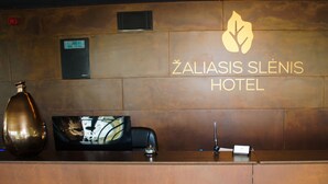 A reception desk at the Zaliasis Slénis Hotel with a clock, a vase, and a small bottle of perfume. - Zaliasis slenis - Self check-in hotel (Aukštkiemiai)