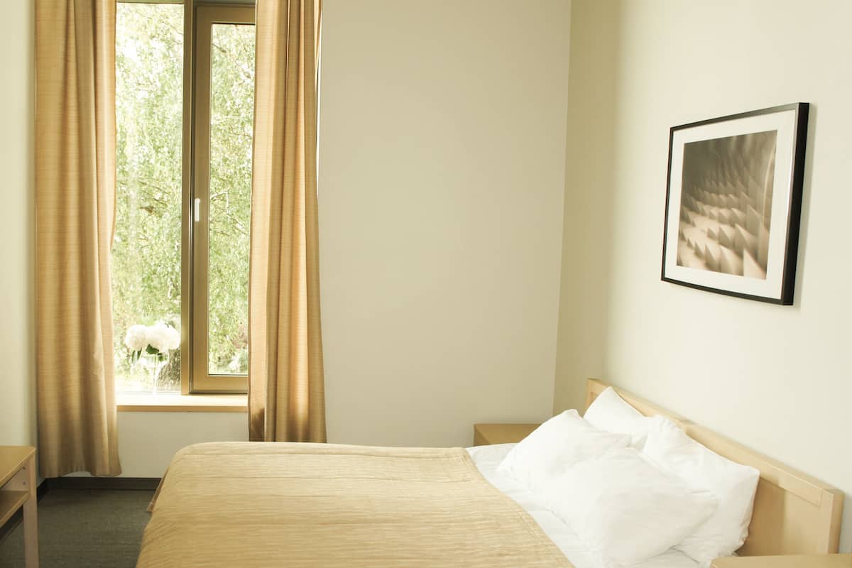 Ein Hotelzimmer mit einem Bett, einem Nachttisch, einem Fenster mit Vorhängen und einem gerahmten Bild an der Wand.