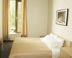 Una habitación de hotel con cama, mesita de noche, ventana con cortinas e imagen enmarcadas en la pared.