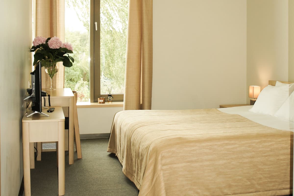Ein Hotelzimmer mit einem Bett, einem Schreibtisch mit Computer, einem Stuhl und einem Vorhangfenster.