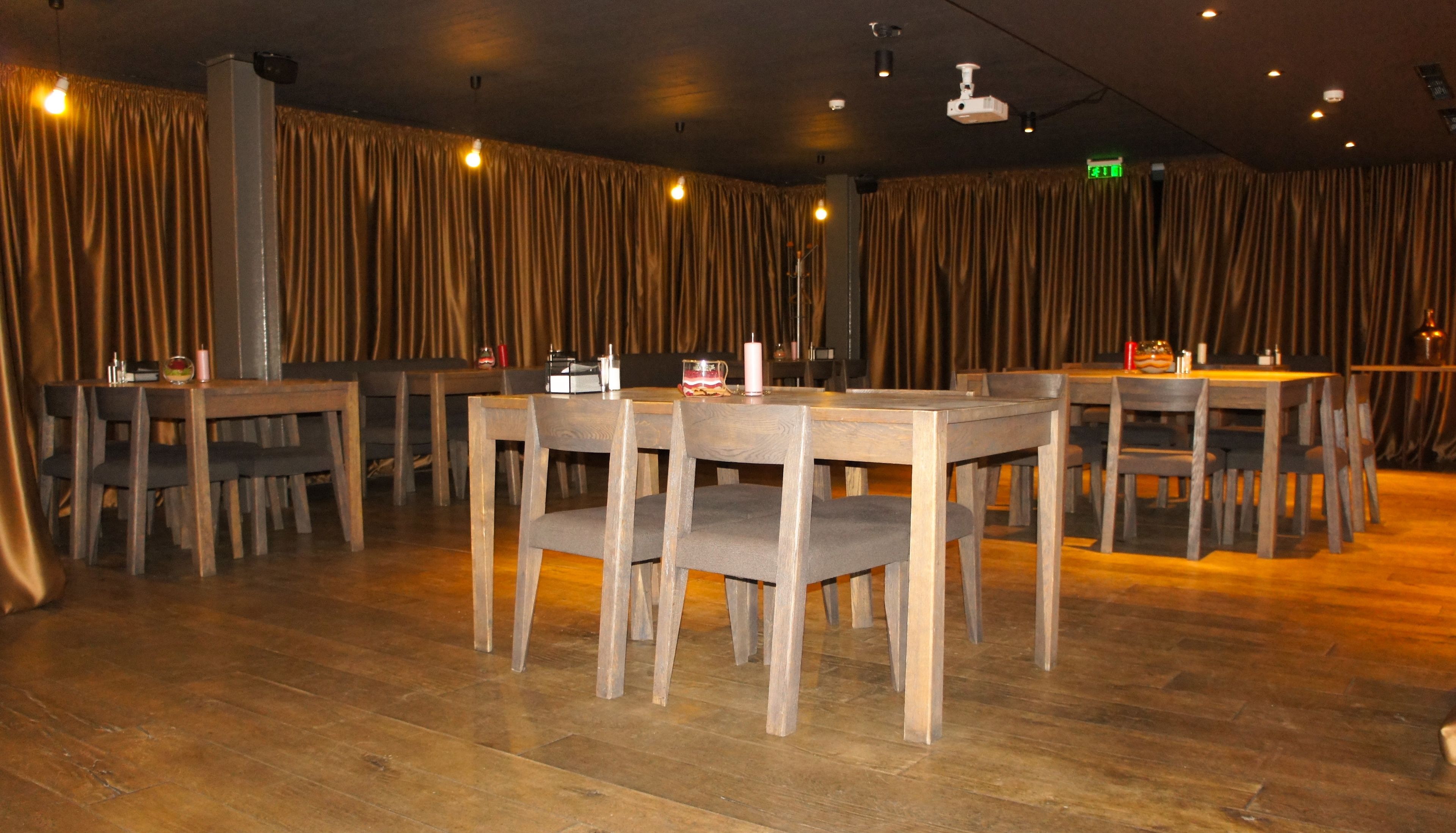 A restaurant with wooden tables and chairs, dim lighting, and curtains.