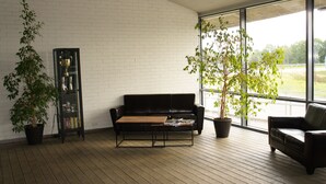 A modern living room with a black leather sofa, a wooden coffee table, and two potted plants. - Zaliasis slenis - Self check-in hotel (Aukštkiemiai)