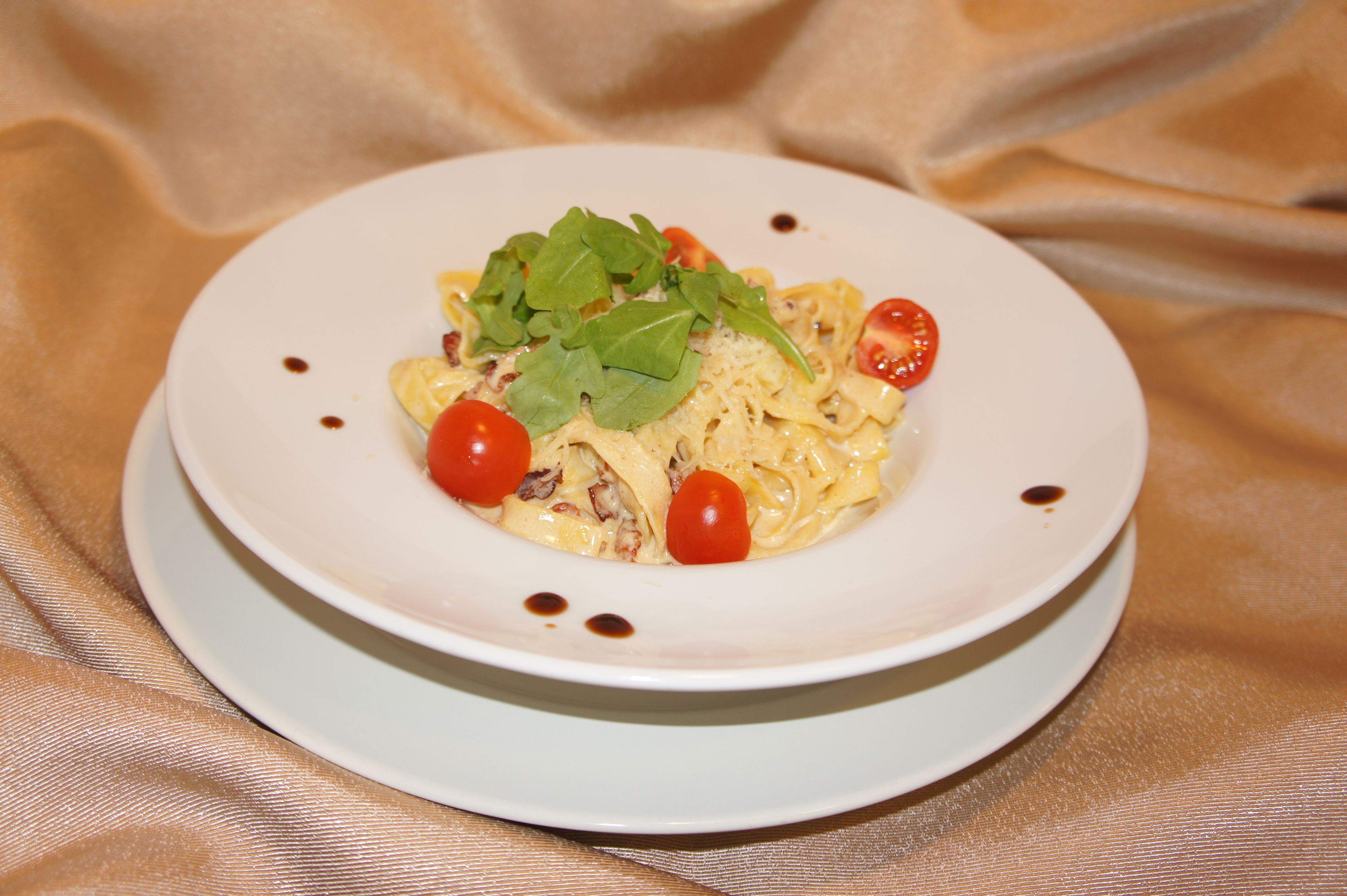 Prato de massa com tomates cereja e folhas verdes sobre um prato branco.
