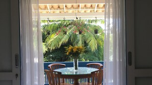 A room with a bed, a table with chairs, and a view of a garden through a door with curtains. - Morada Da Luz (Mata de São João)