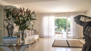 A modern living room with a glass coffee table, a bookshelf, a sofa, and a view of the outdoors through large windows. - Morada Da Luz (Mata de São João)