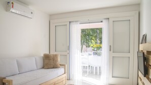 A room with a sofa, a TV, and a sliding door leading to an outdoor area with a table and chairs. - Morada Da Luz (Mata de São João)