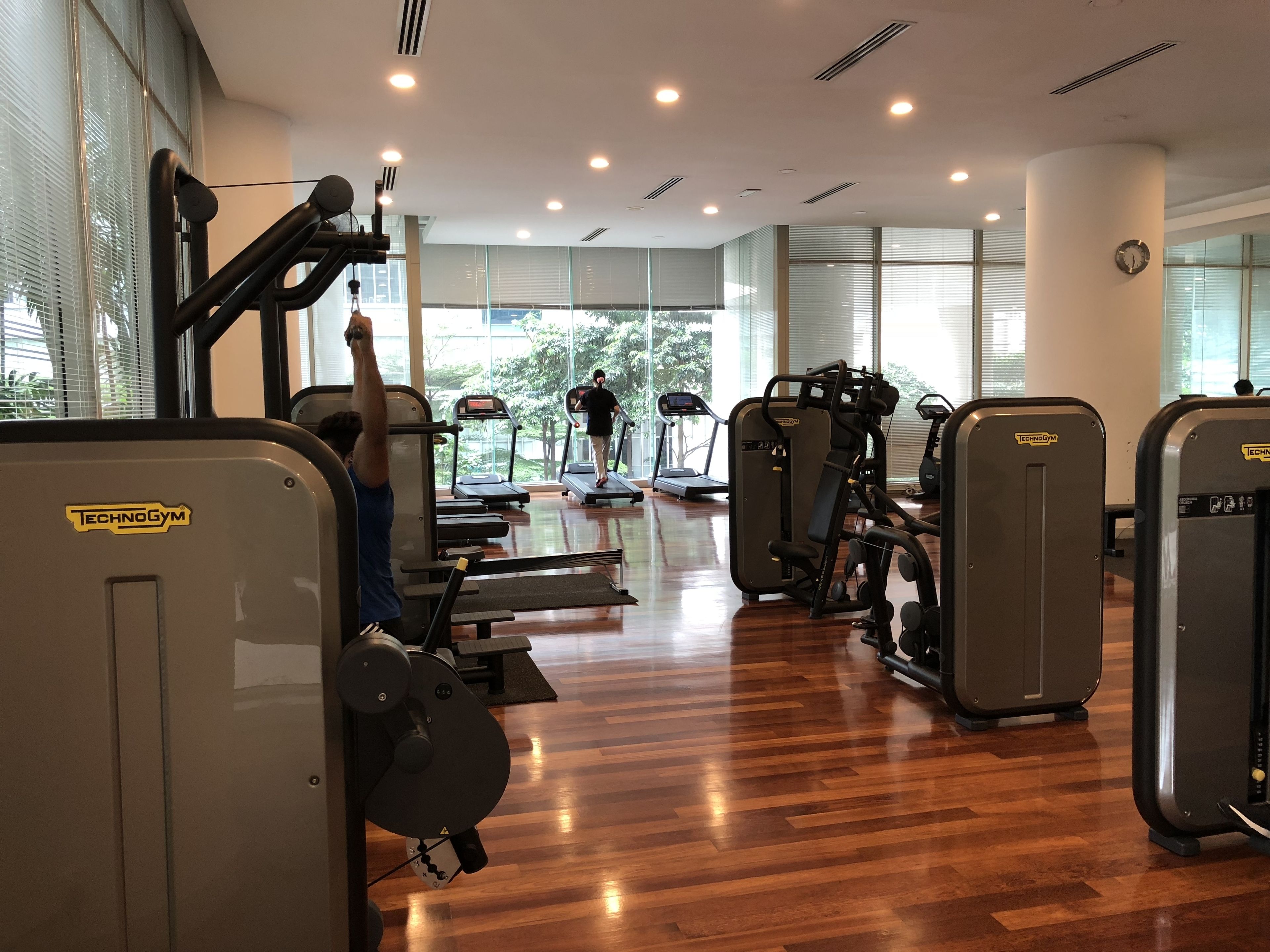 Une salle de sport équipée de tapis de course, d'appareils de musculation et où une personne s'entraîne avec un appareil à câbles.