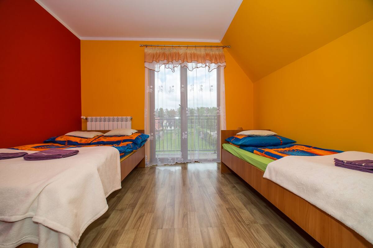 Ein Zimmer mit zwei Betten, einem Fenster mit Vorhang und Blick auf einen Balkon.