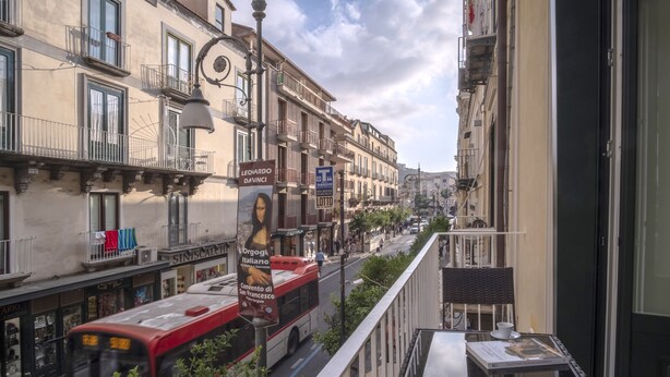 A city street with a red bus, buildings with balconies, and a banner advertising a Leonardo da Vinci exhibition.